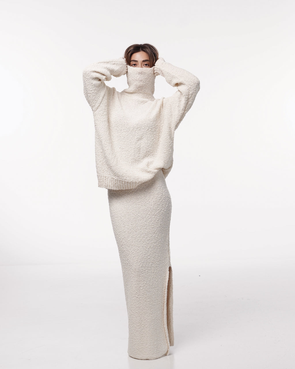 Model wearing a cream oversized turtleneck sweater styled with a matching long knit skirt